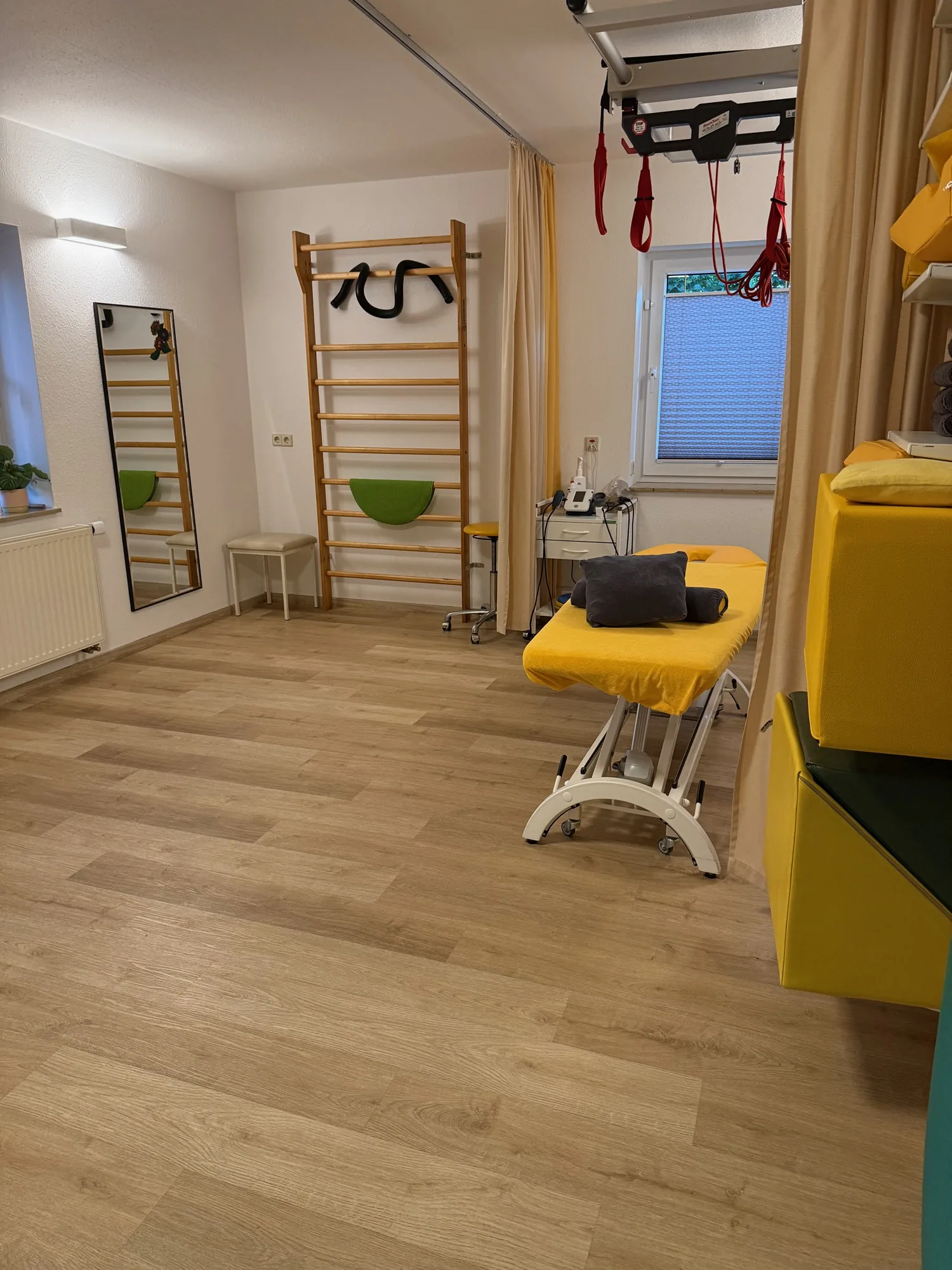 Heller Übungsraum mit Sprossenwand, Spiegel, Schlingentisch und Therapieliege